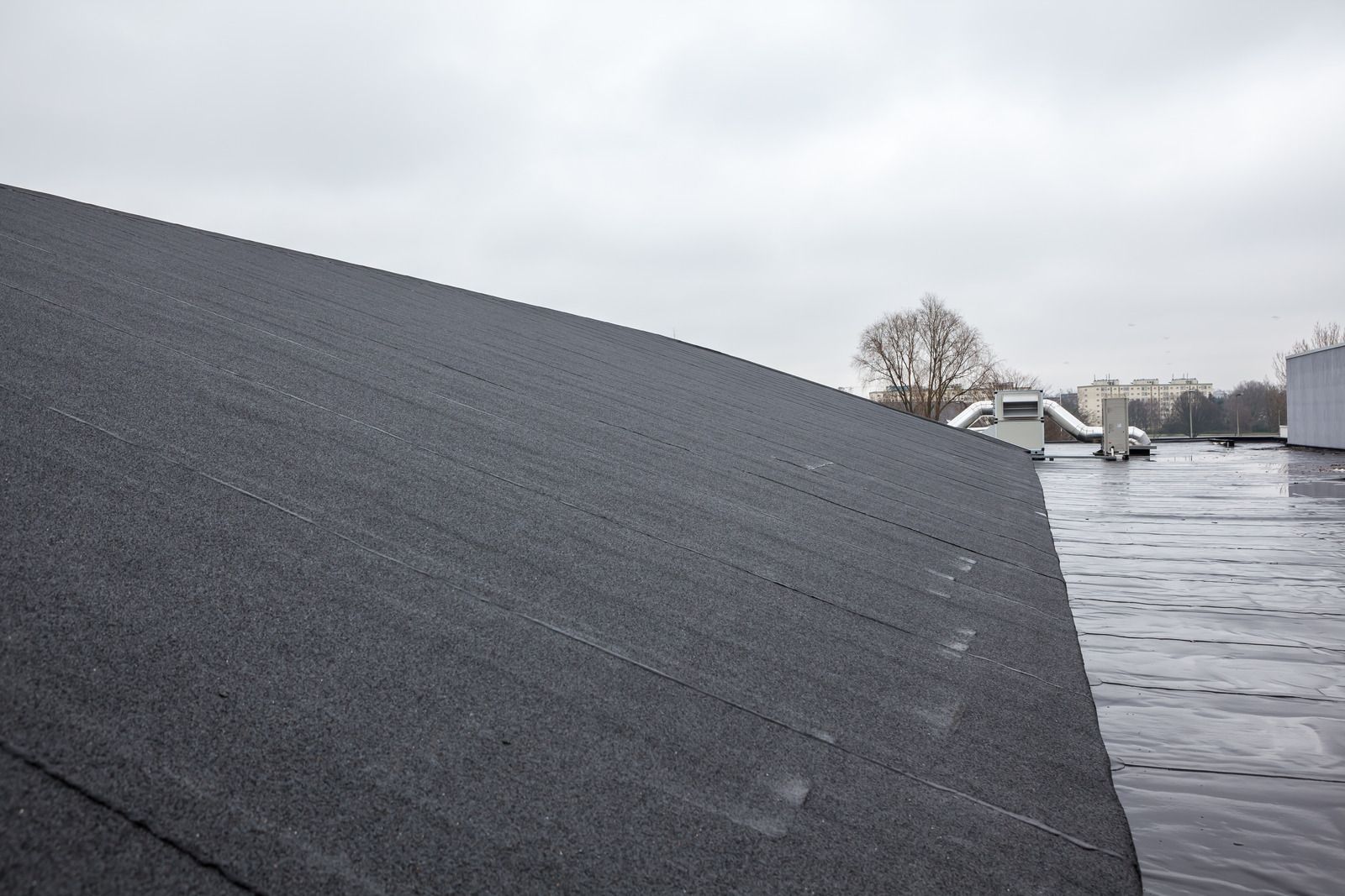 Snow-covered roof with water pooling beside it under a gray sky