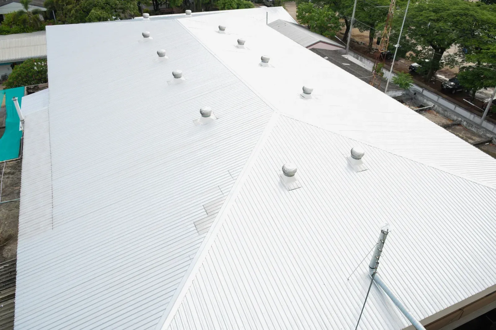 White metal roof viewed from above, with multiple vents and trees at the edge of the building.