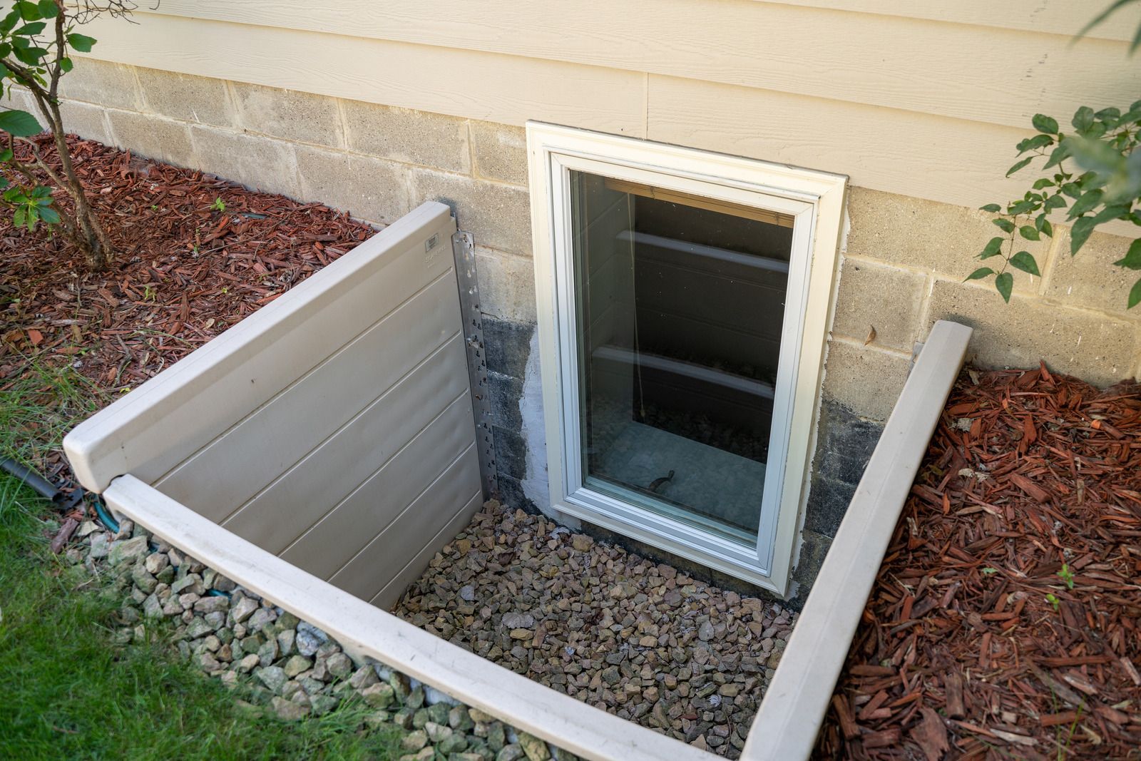 Basement window well with gravel and metal sides against beige house siding
