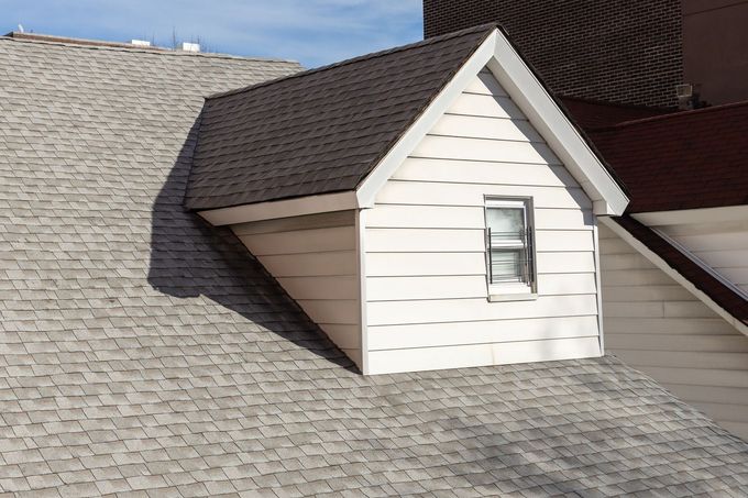 Small white dormer on a gray shingled roof in sunlight