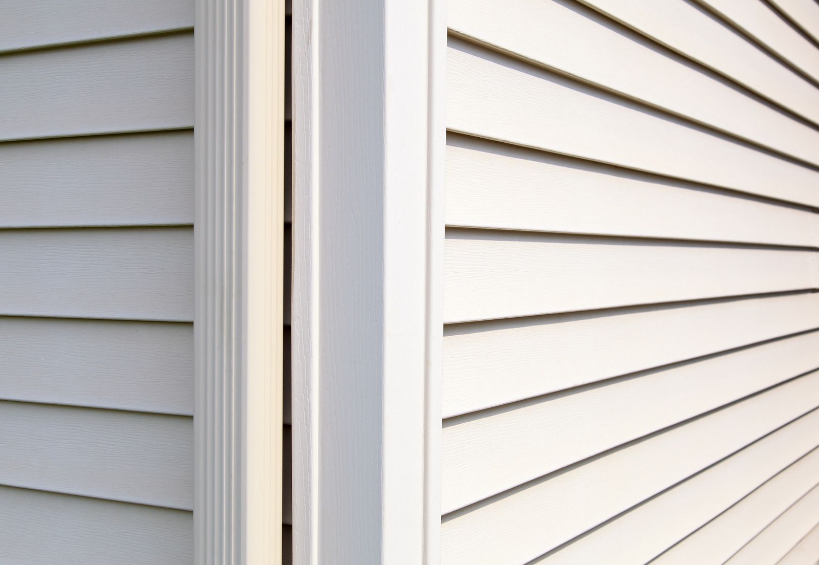 Close-up of white house siding and trim at an exterior corner with a narrow gap between panels