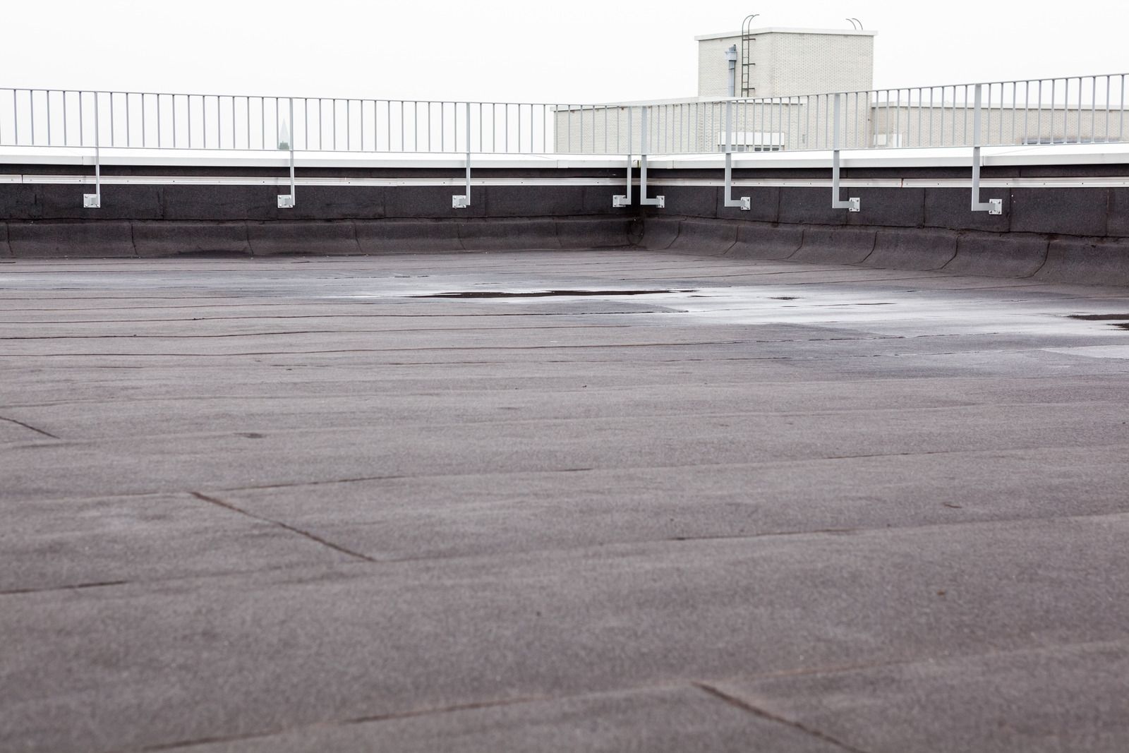 Empty rooftop with wet pavement and a white railing under an overcast sky.