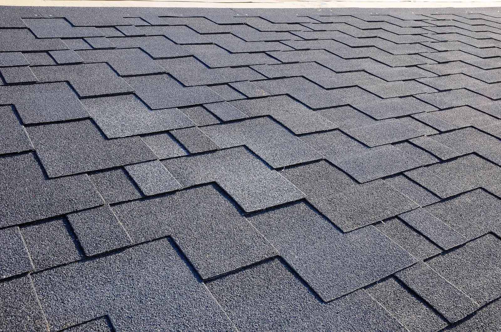 Close-up of gray asphalt roof shingles with a repeating zigzag pattern