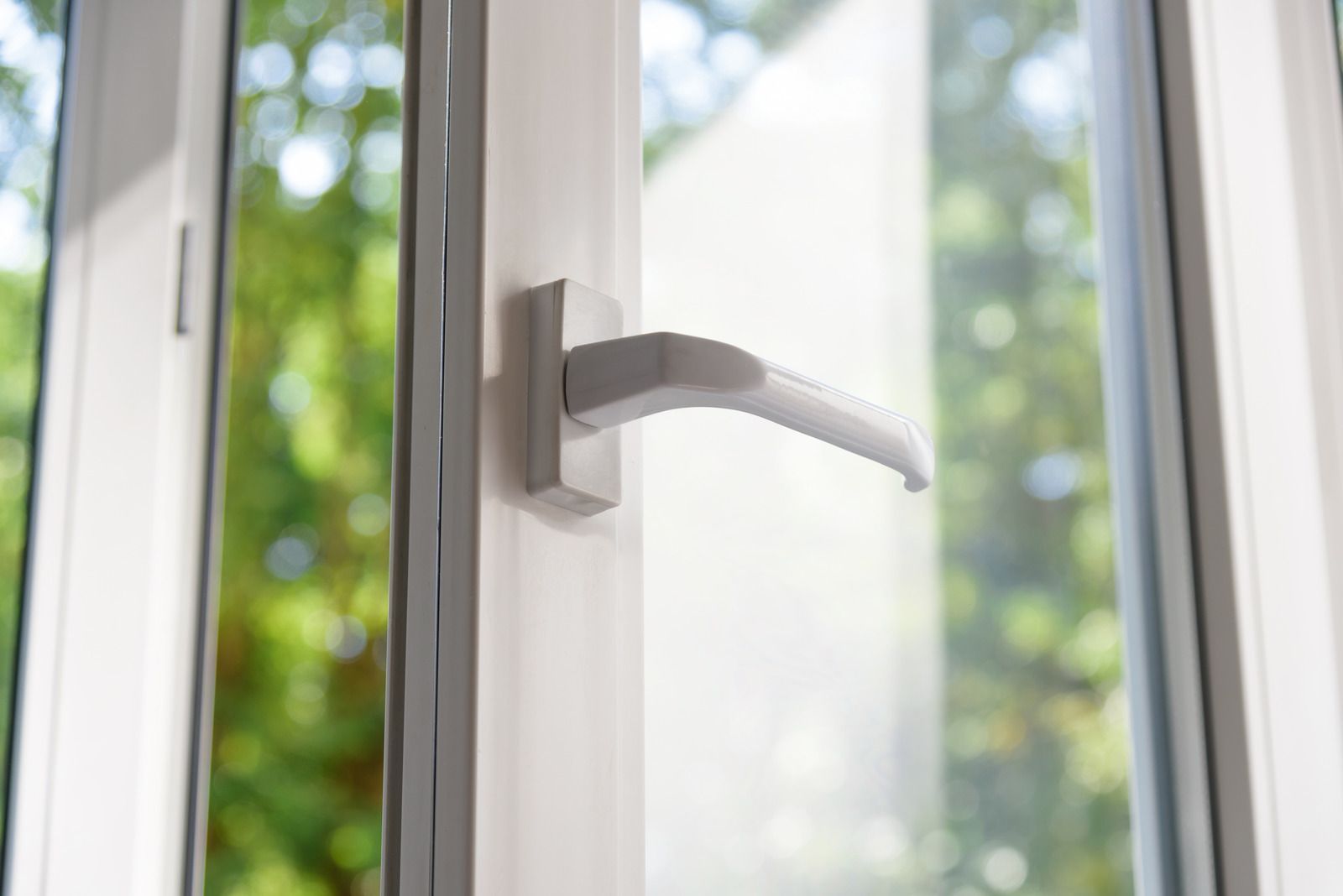 White window handle on an open window with blurred greenery outside