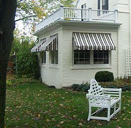 White brick house with awnings, a balcony, and a bench in a yard