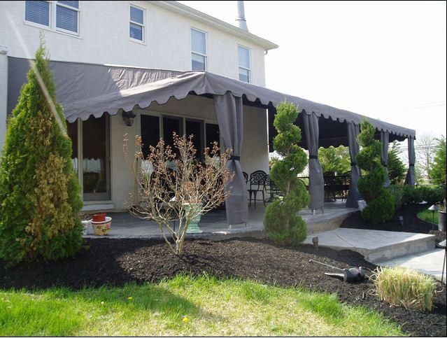 Backyard patio with dark awning, surrounded by trees and black mulch
