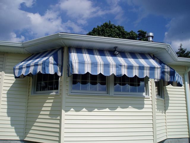 Blue and white striped awnings over windows on a light yellow house against a cloudy sky