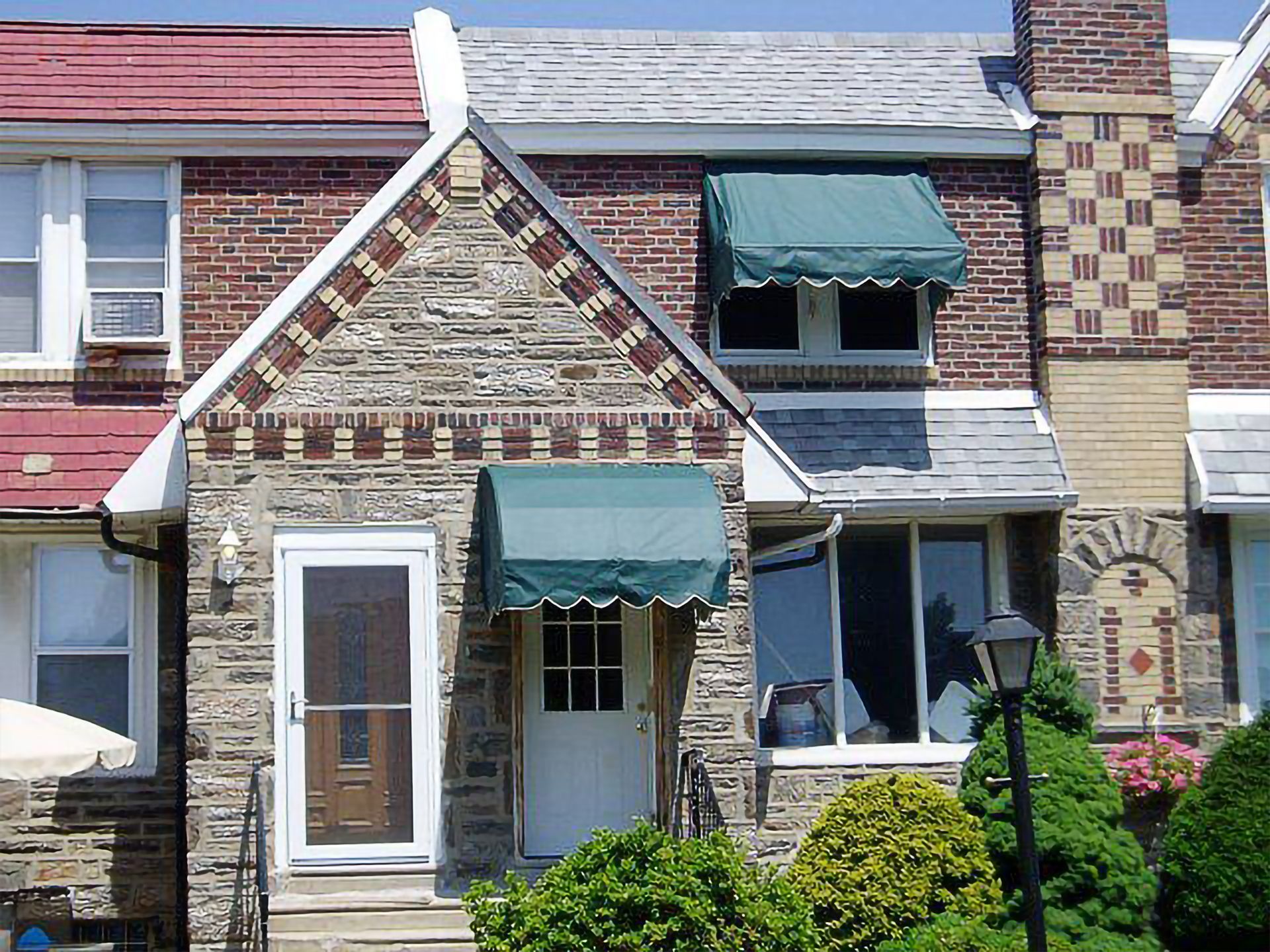 Row house with stone and brick facade, green awnings, and white doors