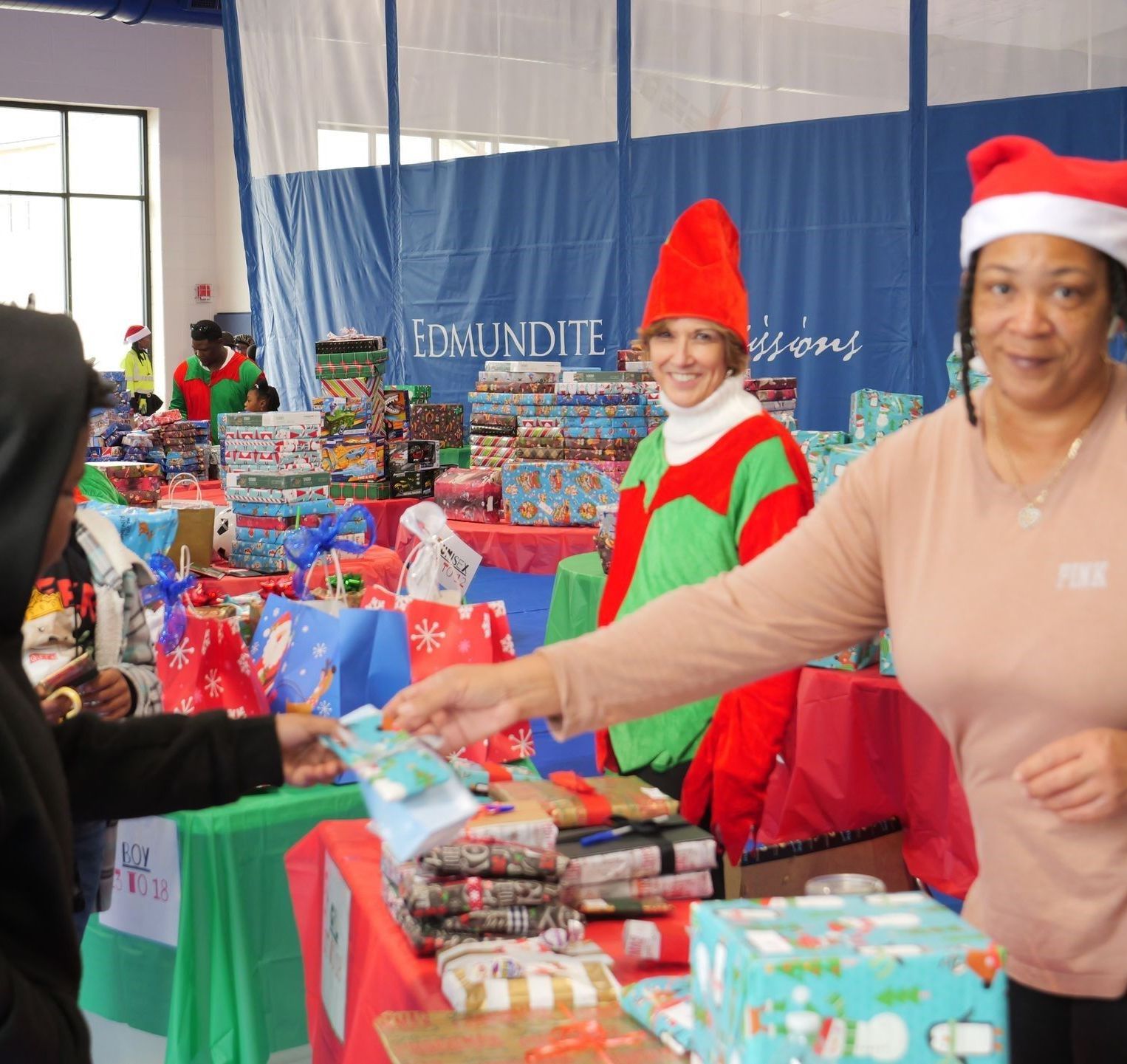 A woman wearing a santa hat is standing in front of a table full of gifts