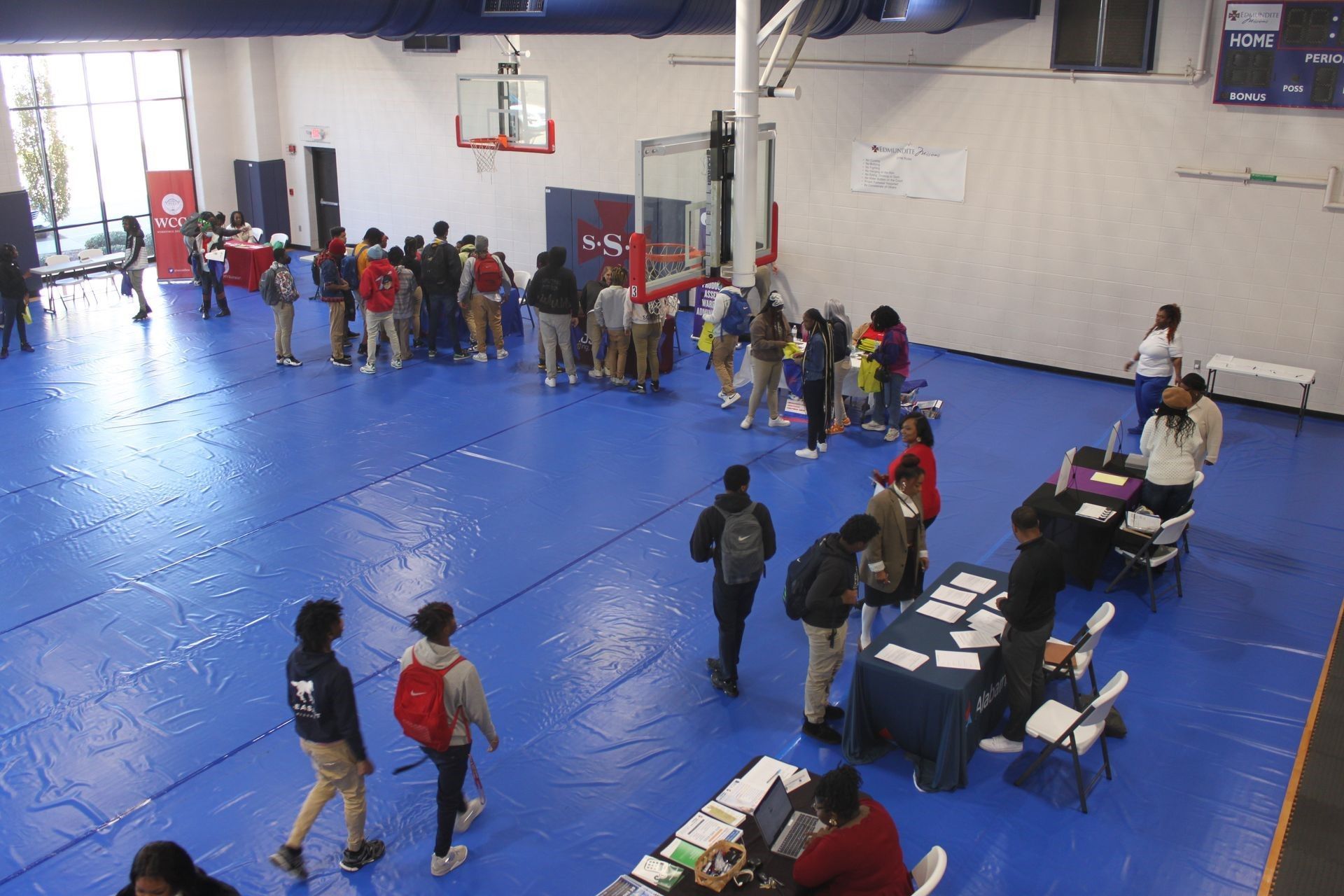 A group of people are standing around tables in a gym