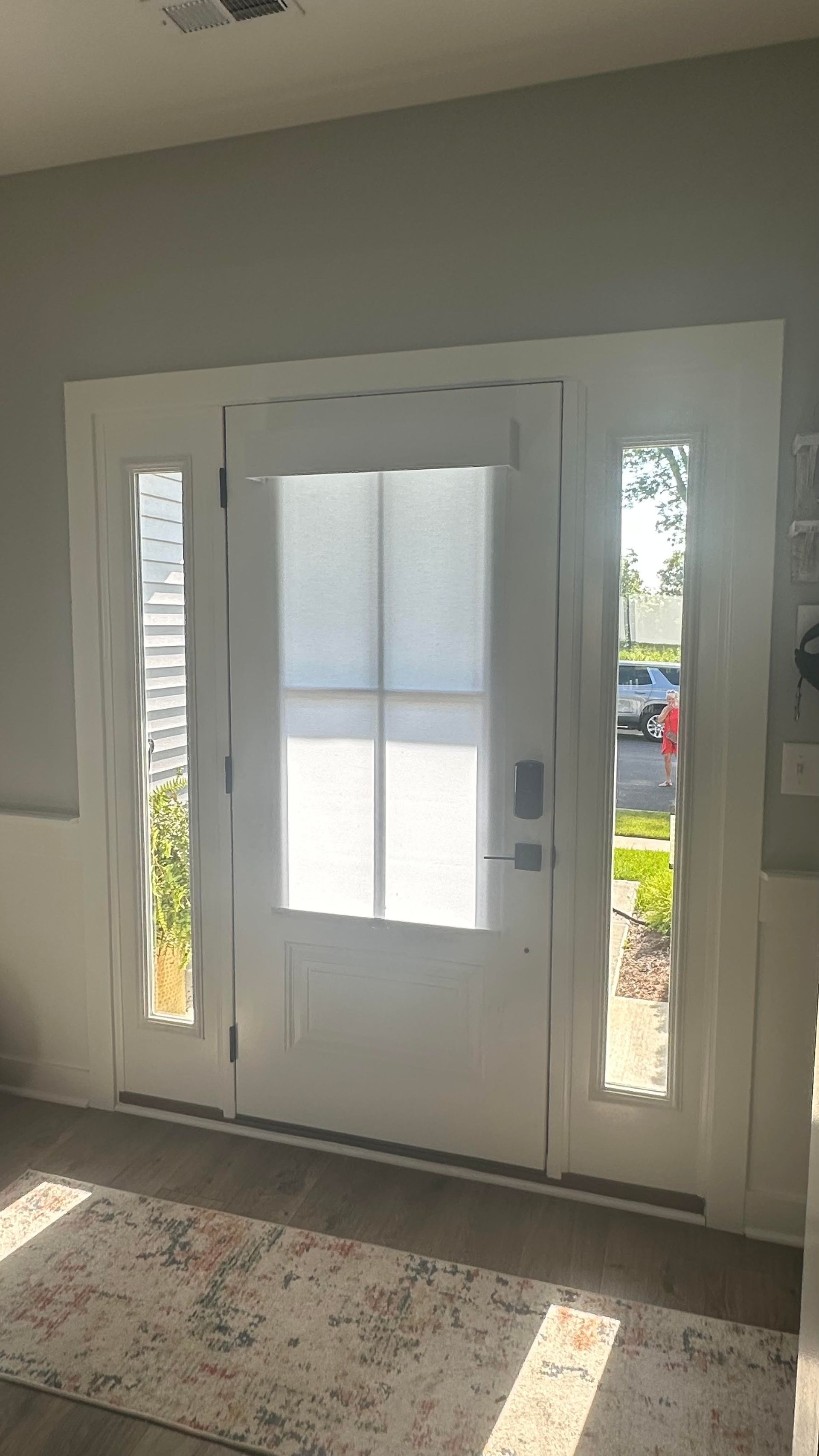 White front door with glass panels on the sides, featuring a privacy-covered window and interior floor mat.