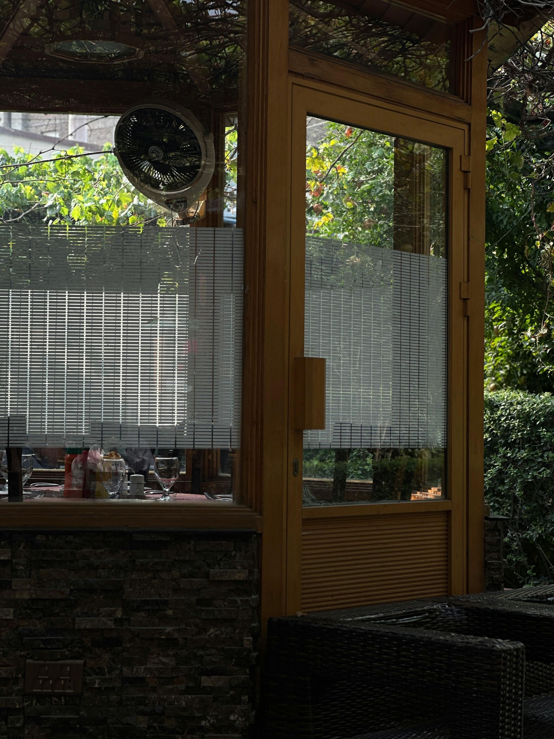 Wooden structure with glass door and window overlooking a garden; wicker furniture in the foreground.