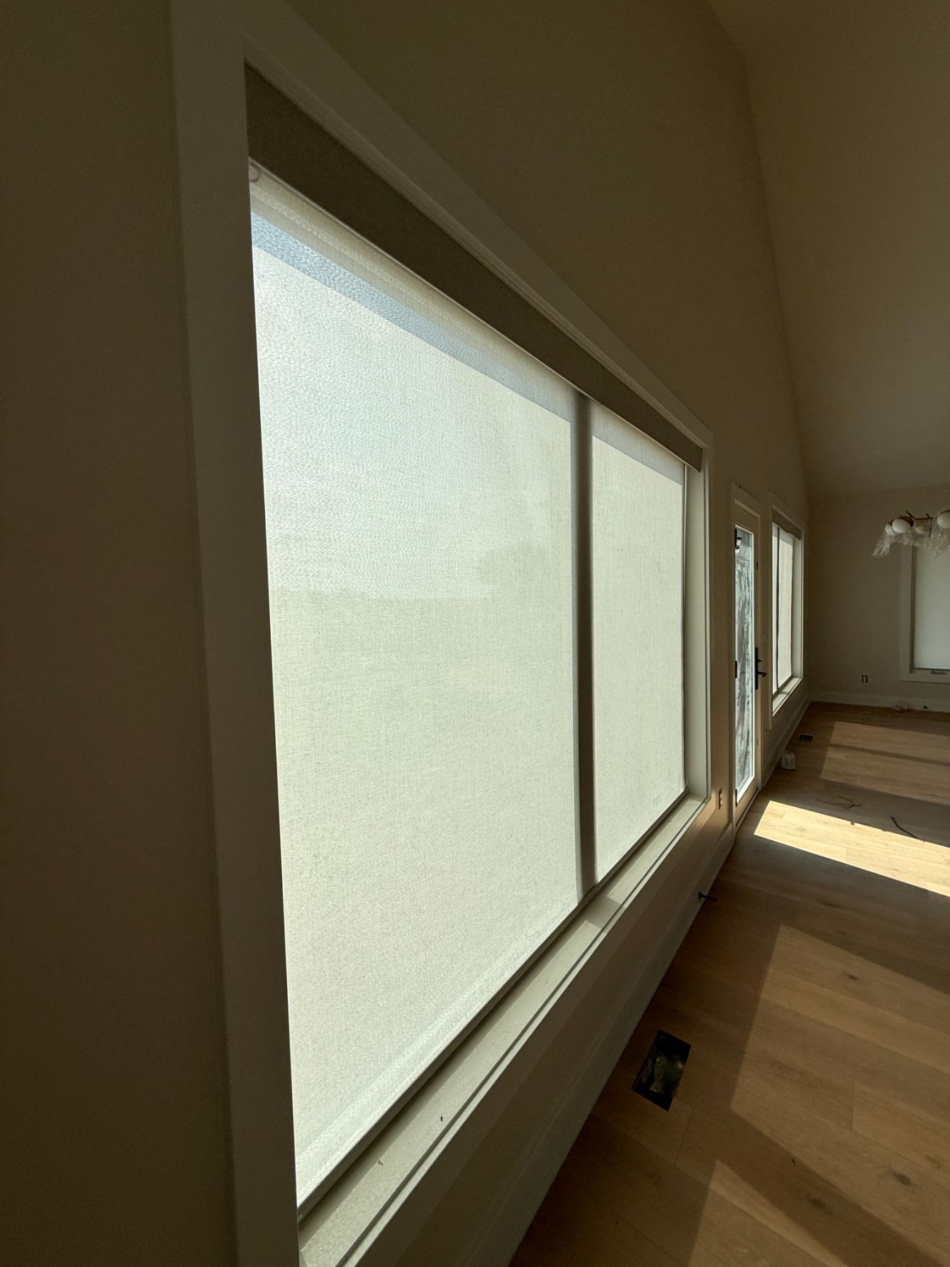 Bright sunlit room with large windows with roller shades and light wood floors.