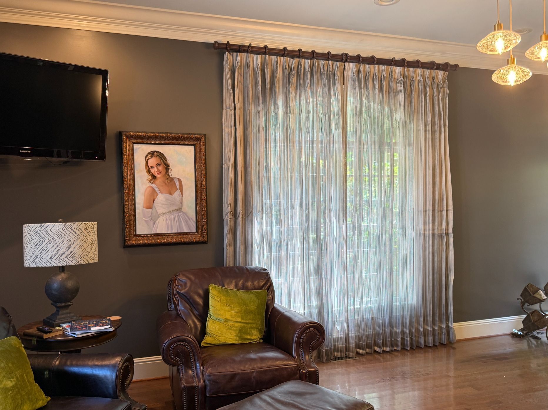 Living room with leather chair, lamp, wall art, TV, and sheer curtains over a bright window.