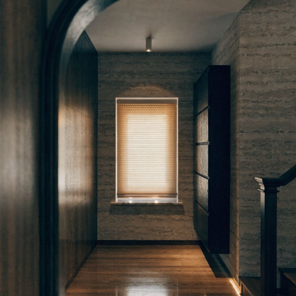 Narrow hallway with wood floor, textured walls, and a sunlit window with blinds at the end.