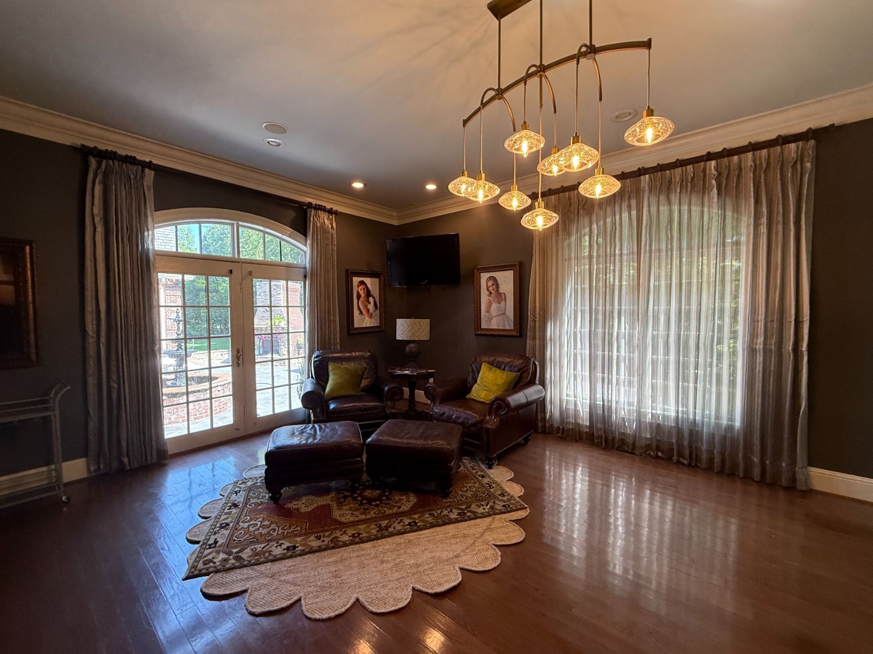 Elegant living room with dark wood floors, chandelier, large windows, and a central seating area on a rug
