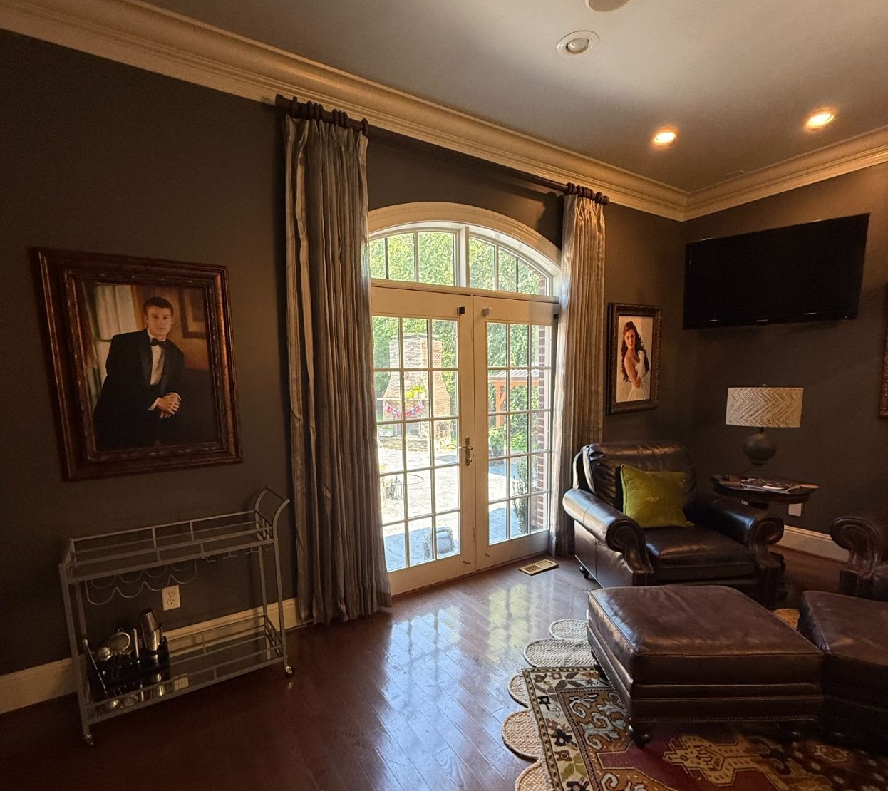 Elegant living room with French doors, dark furniture, custom drapery, framed portraits, and warm recessed lighting