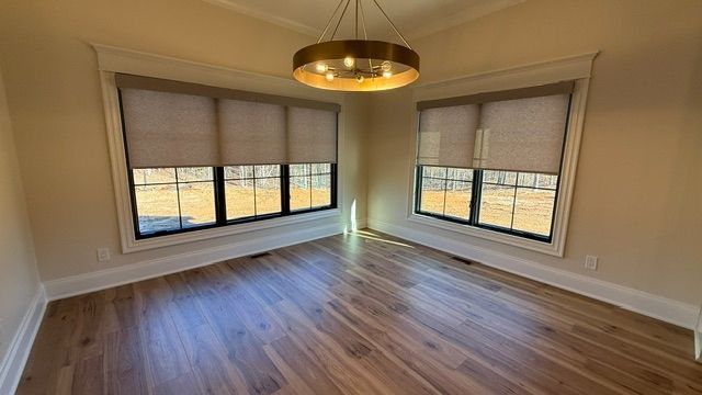 Empty modern room with wood floors, large windows, beige walls, and a brass ceiling light.