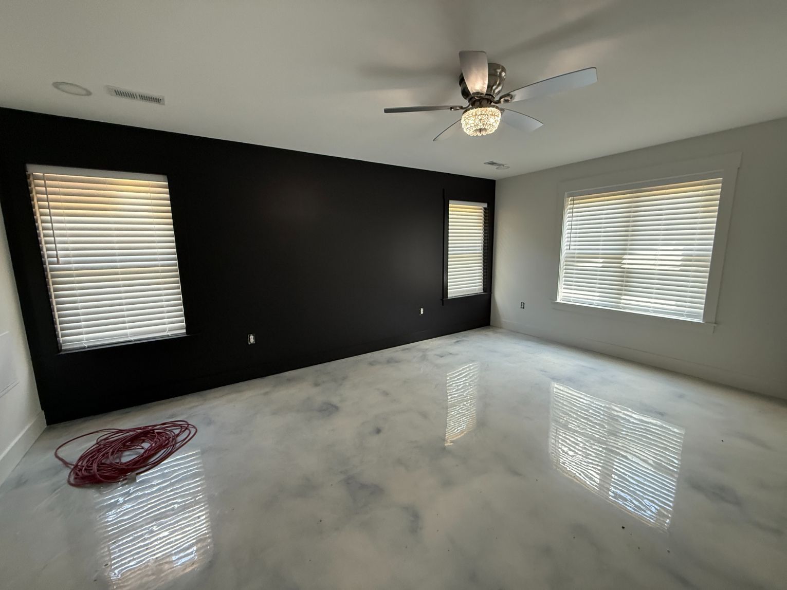 Empty modern room with glossy white floor, black accent wall, windows, and shutters.