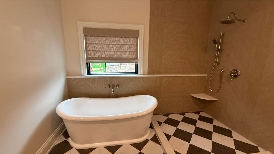 Small bathroom with a freestanding tub, tan walls, a window with , and black-and-white checkered floor.