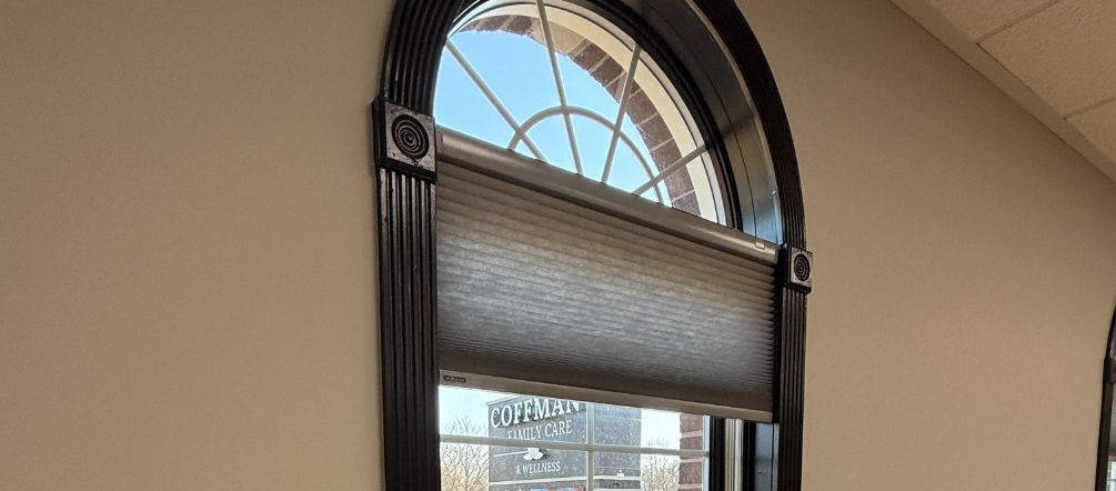Arched window with closed blinds and sunlight filtering into a beige room.