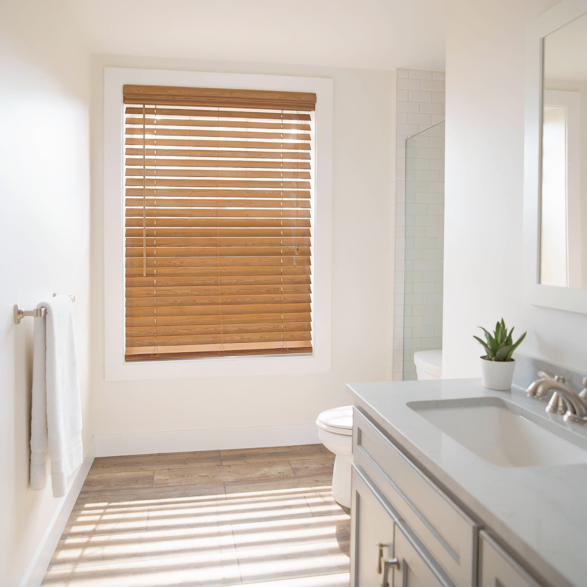 Bright bathroom with a gray vanity, white sink, wooden blinds, and sunlight casting striped shadows on the floor.