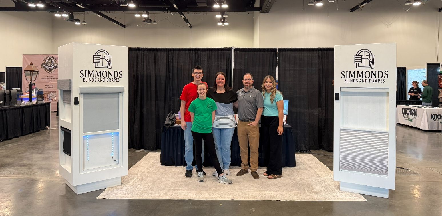 The Simmonds family posing at an Owensboro tradeshow booth with white displays and branded banners.