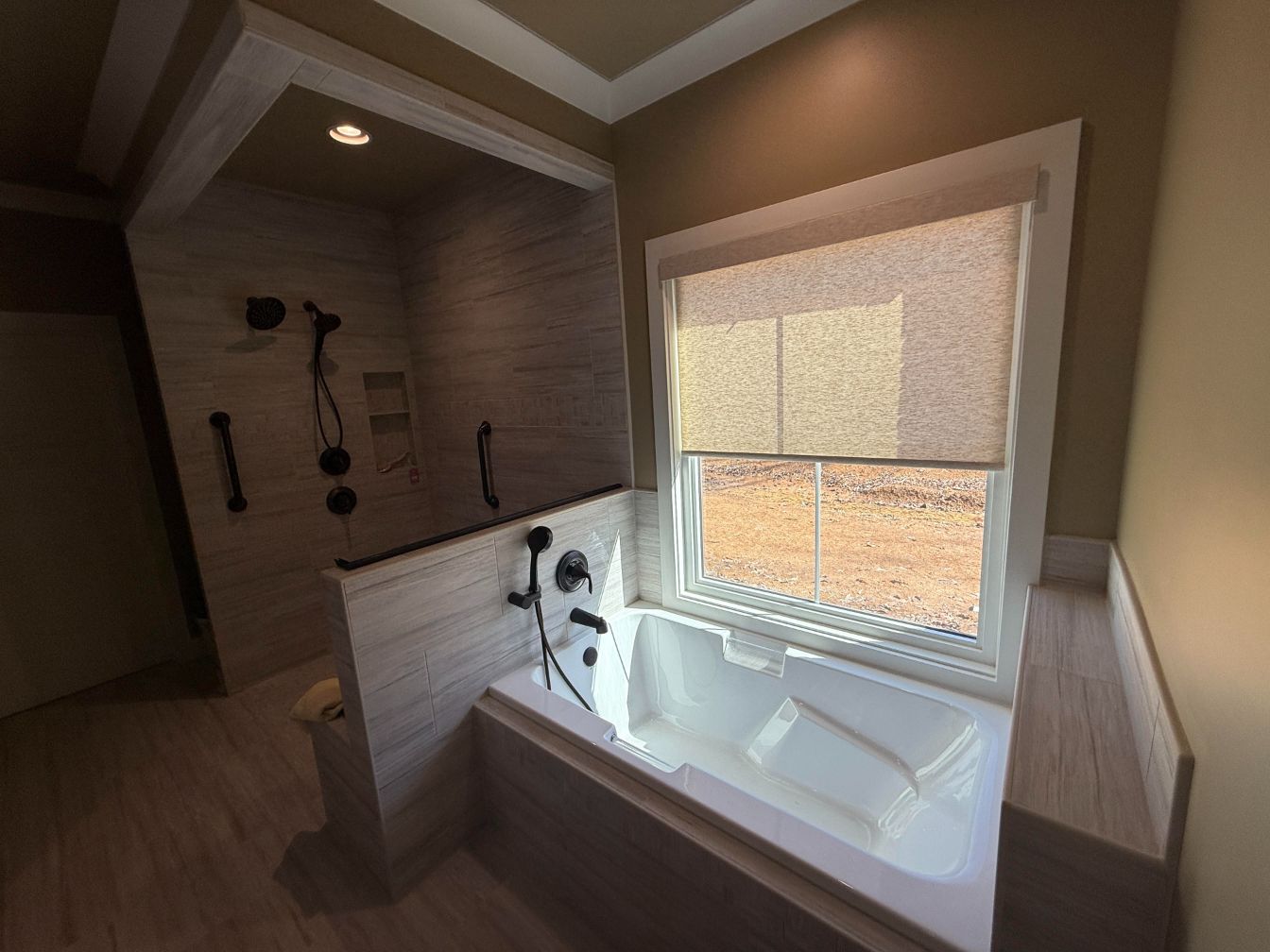 Modern bathroom featuring a walk-in tiled shower with grab bars next to a soaking tub positioned beneath a window.