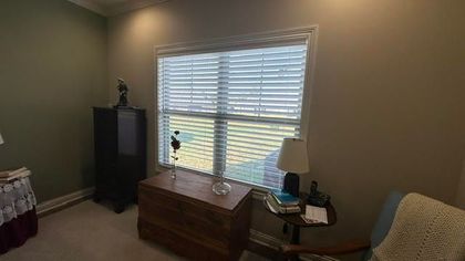 Room with window, blinds, and various furniture like a chest, table, and armchair; green and tan walls.