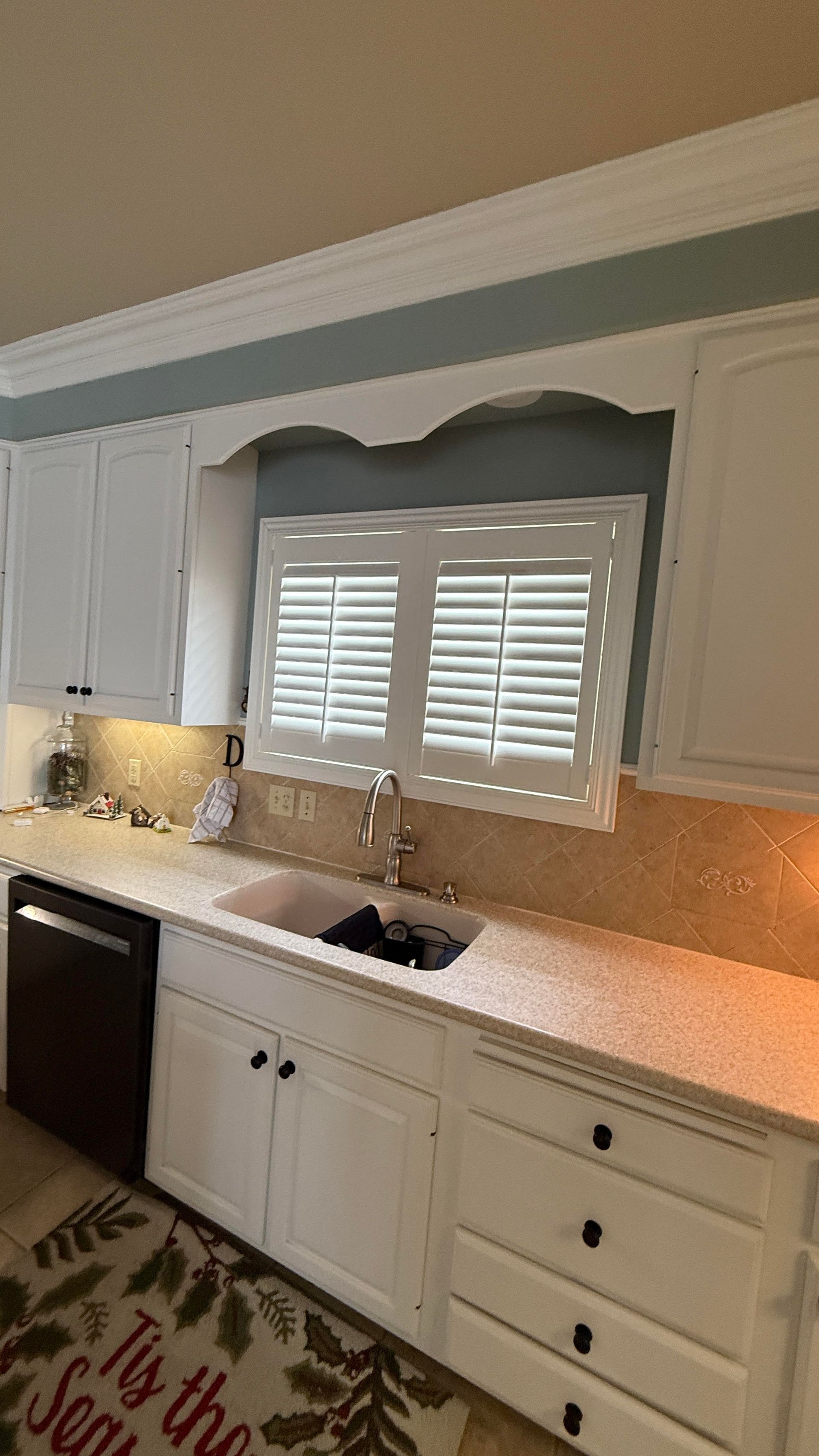 White kitchen with cabinets, sink, and shutters above a countertop.