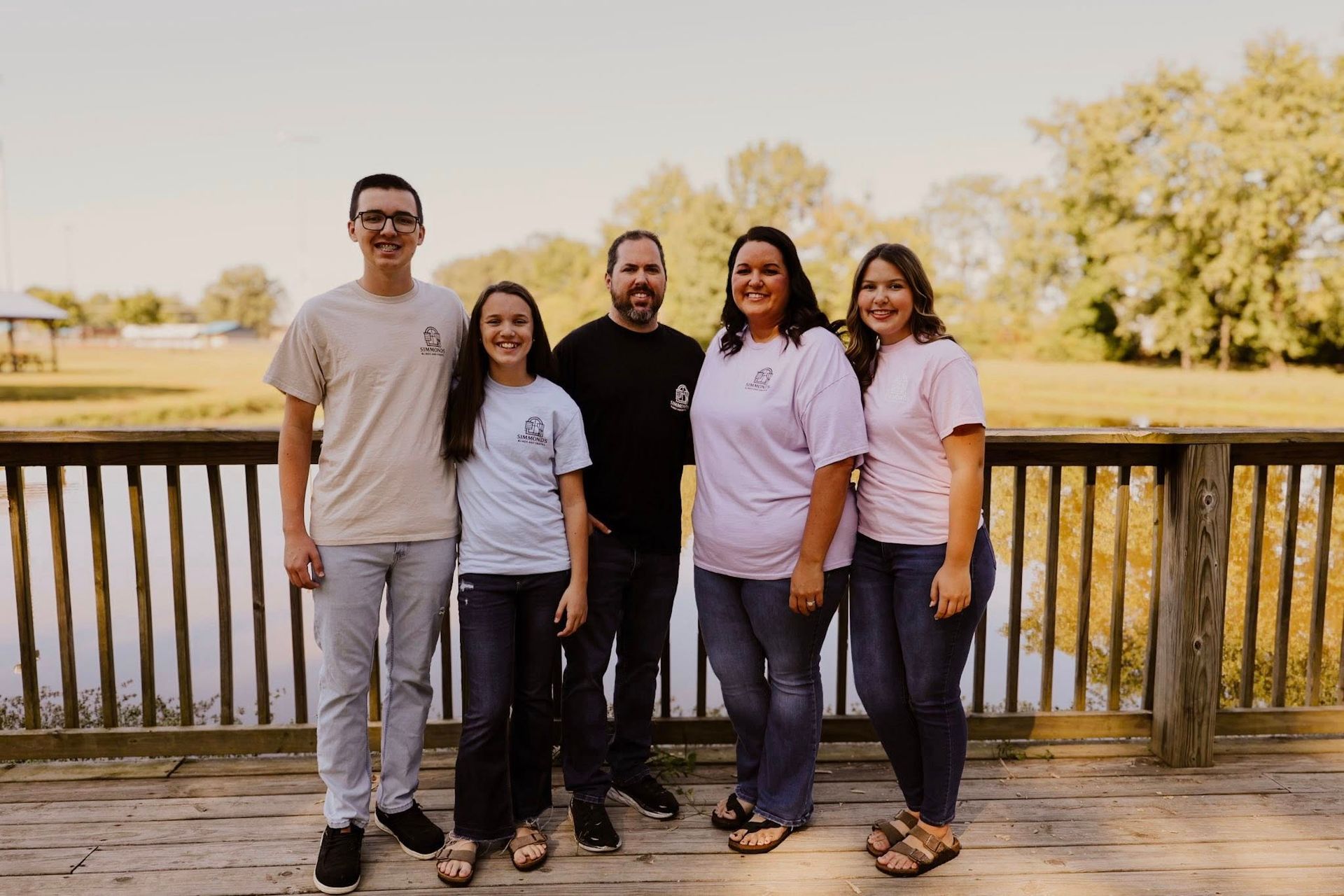 Family of five stands on a wooden dock by a lake, wearing casual clothing.