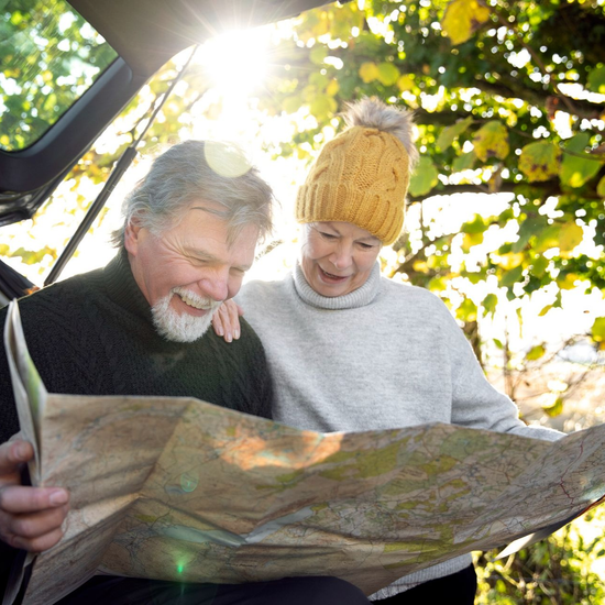 Two people outdoors studying a folded map in bright sunlight under autumn leaves