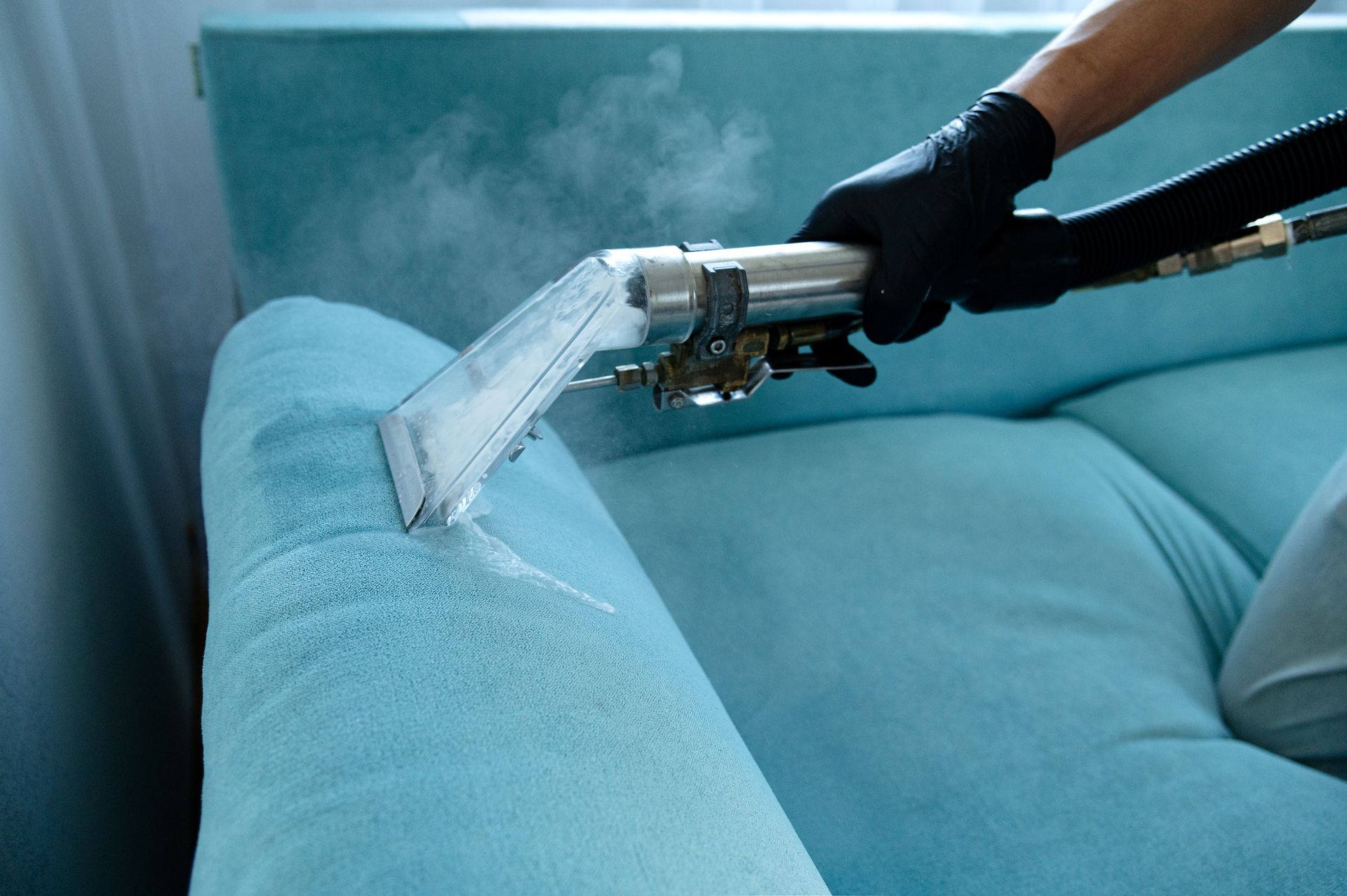 Steam-cleaning a blue couch cushion with a handheld upholstery cleaner