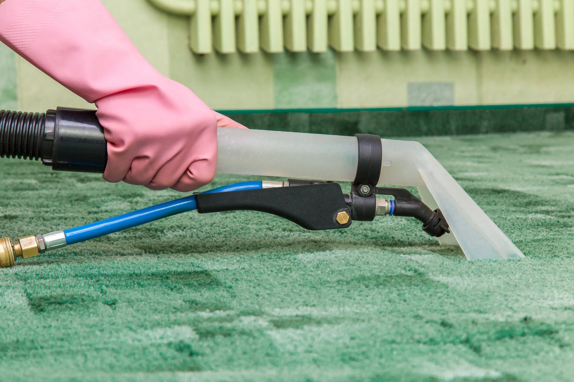 Person using a pressure washer on green carpet, spraying water at a corner edge