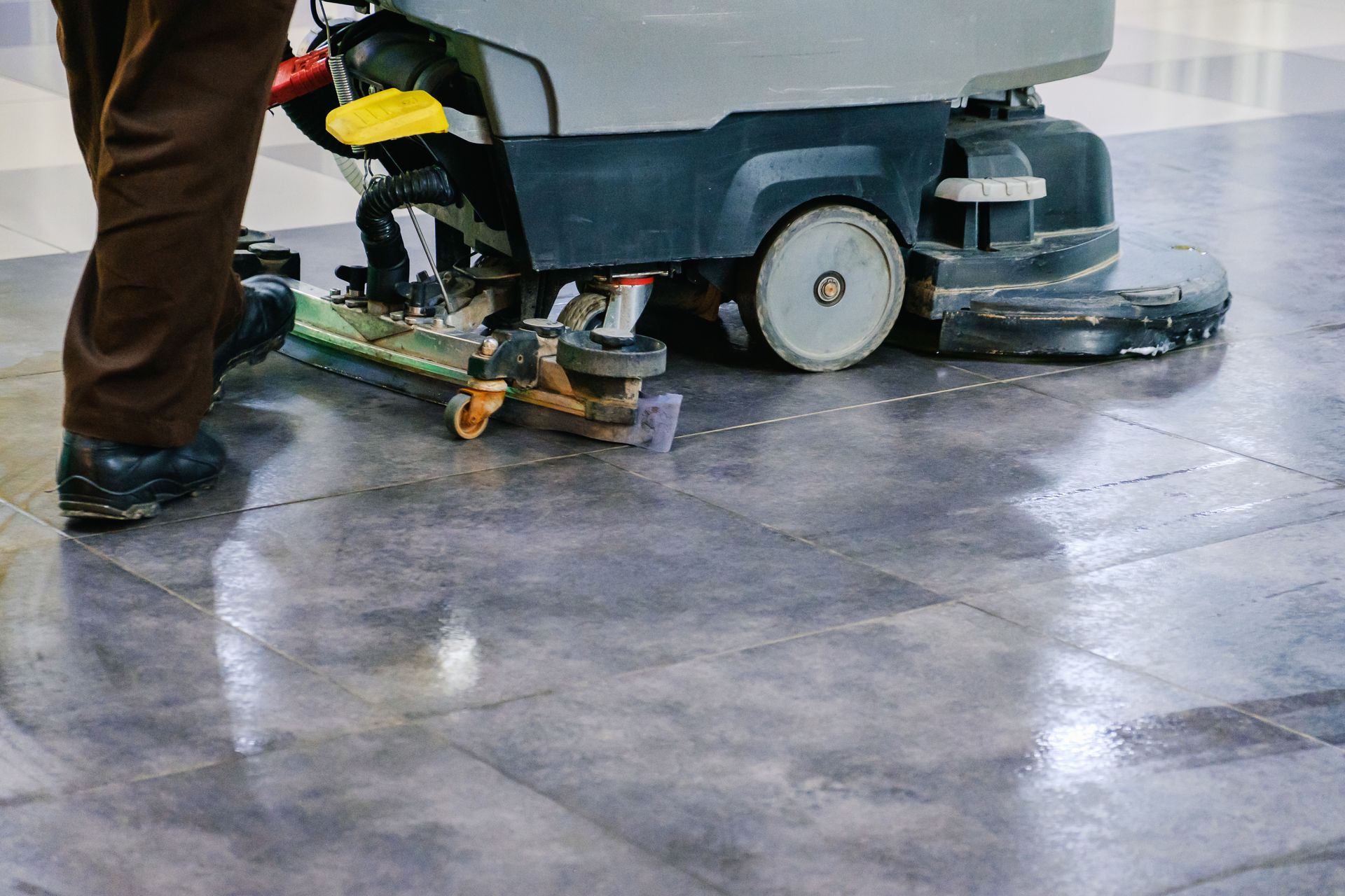 Person operating a floor scrubber on a wet concrete floor.