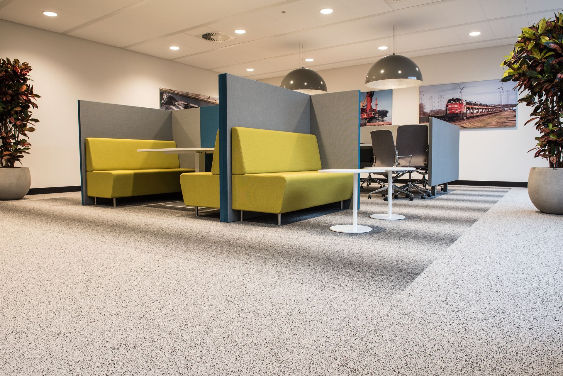 Modern office lounge with yellow chairs, gray carpet, and desks under bright ceiling lights