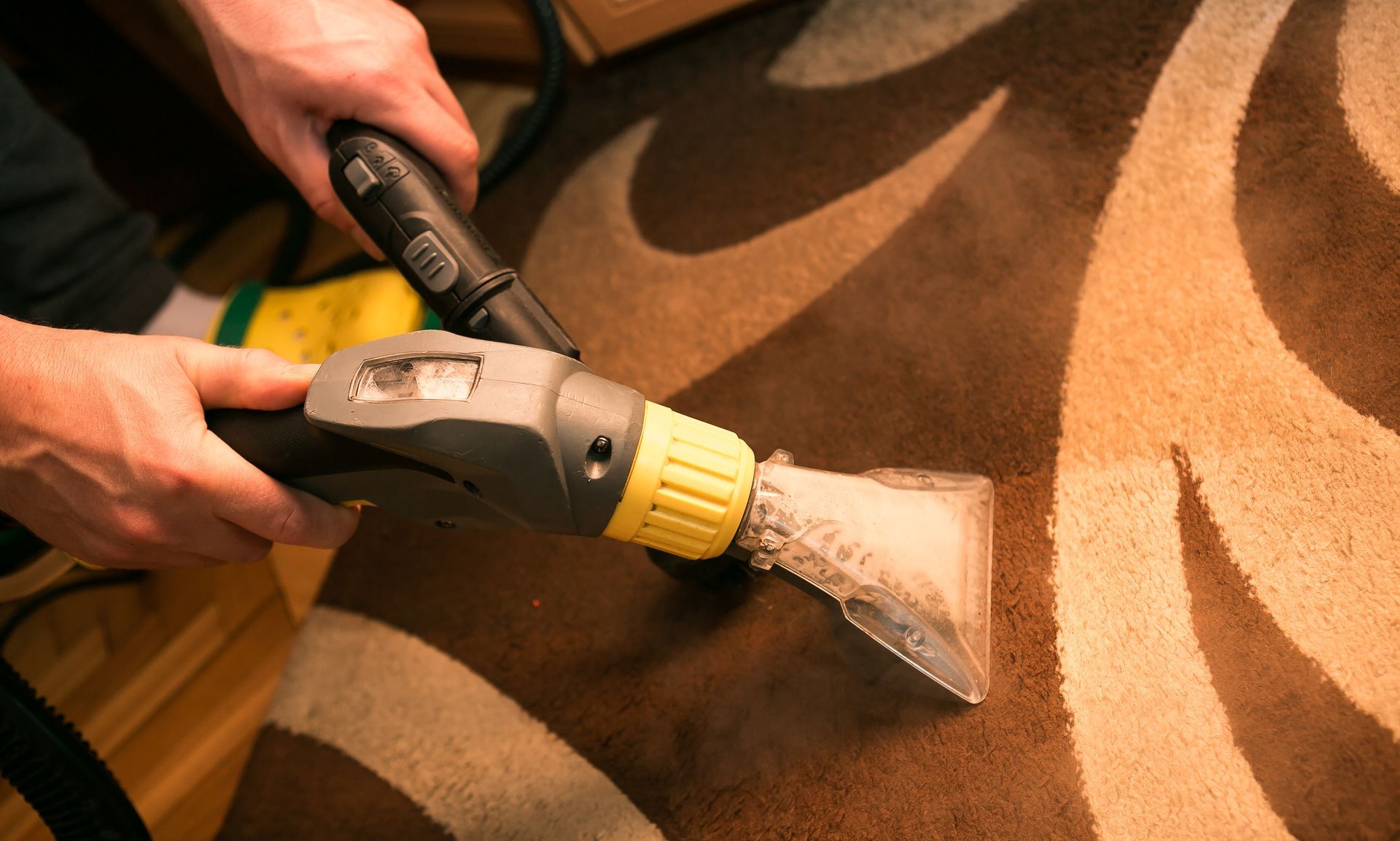 Hands using a steam cleaner on a brown carpet, removing stains. Hands using a steam cleaner on a brown carpet, removing stains.