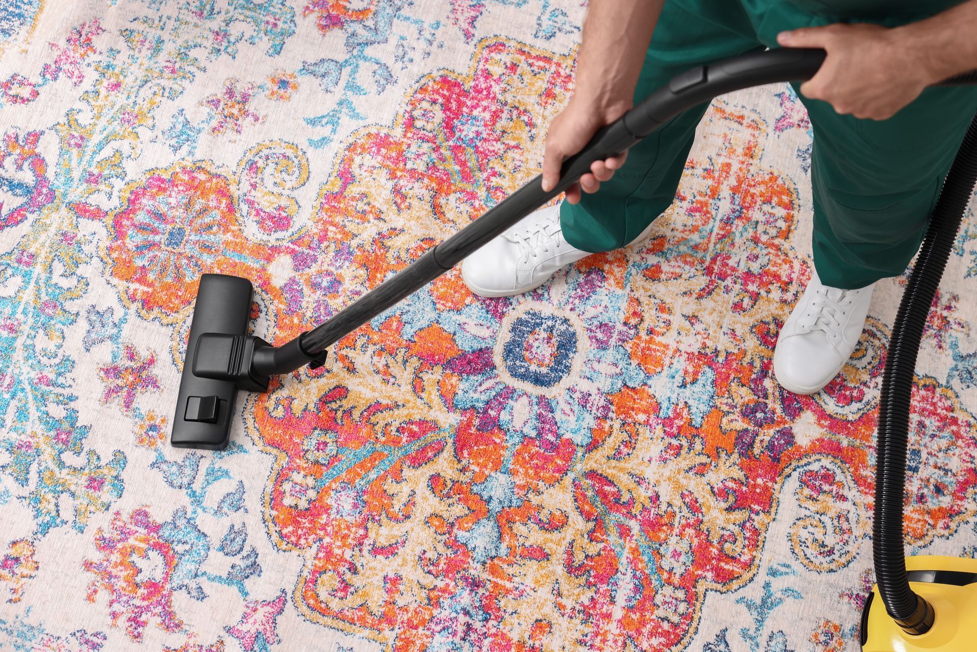 Vacuum cleaning a colorful patterned rug with a black vacuum and hose