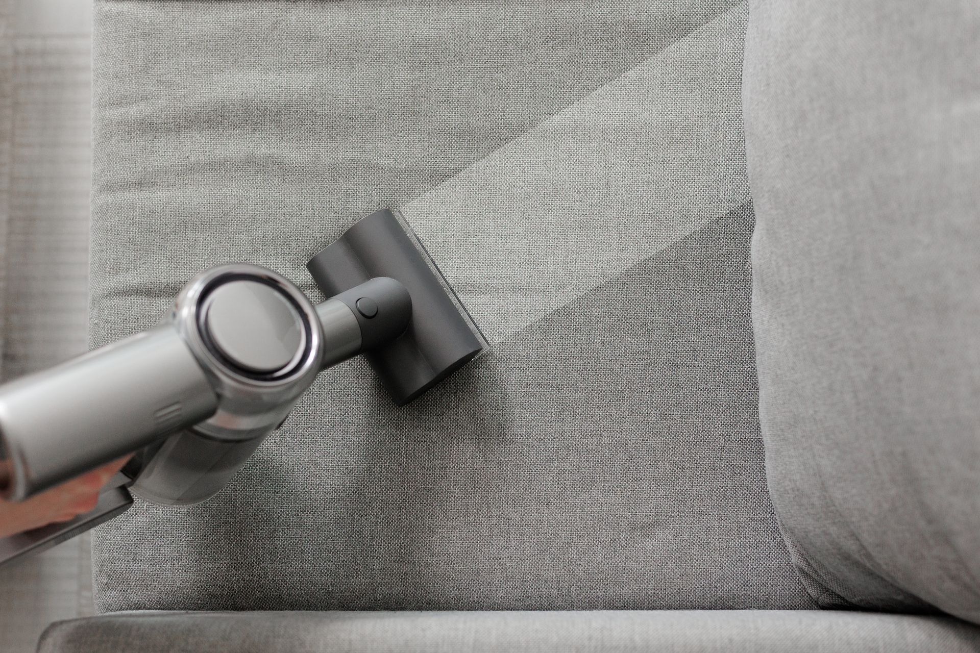 Handheld vacuum cleaning gray fabric upholstery on a sofa cushion