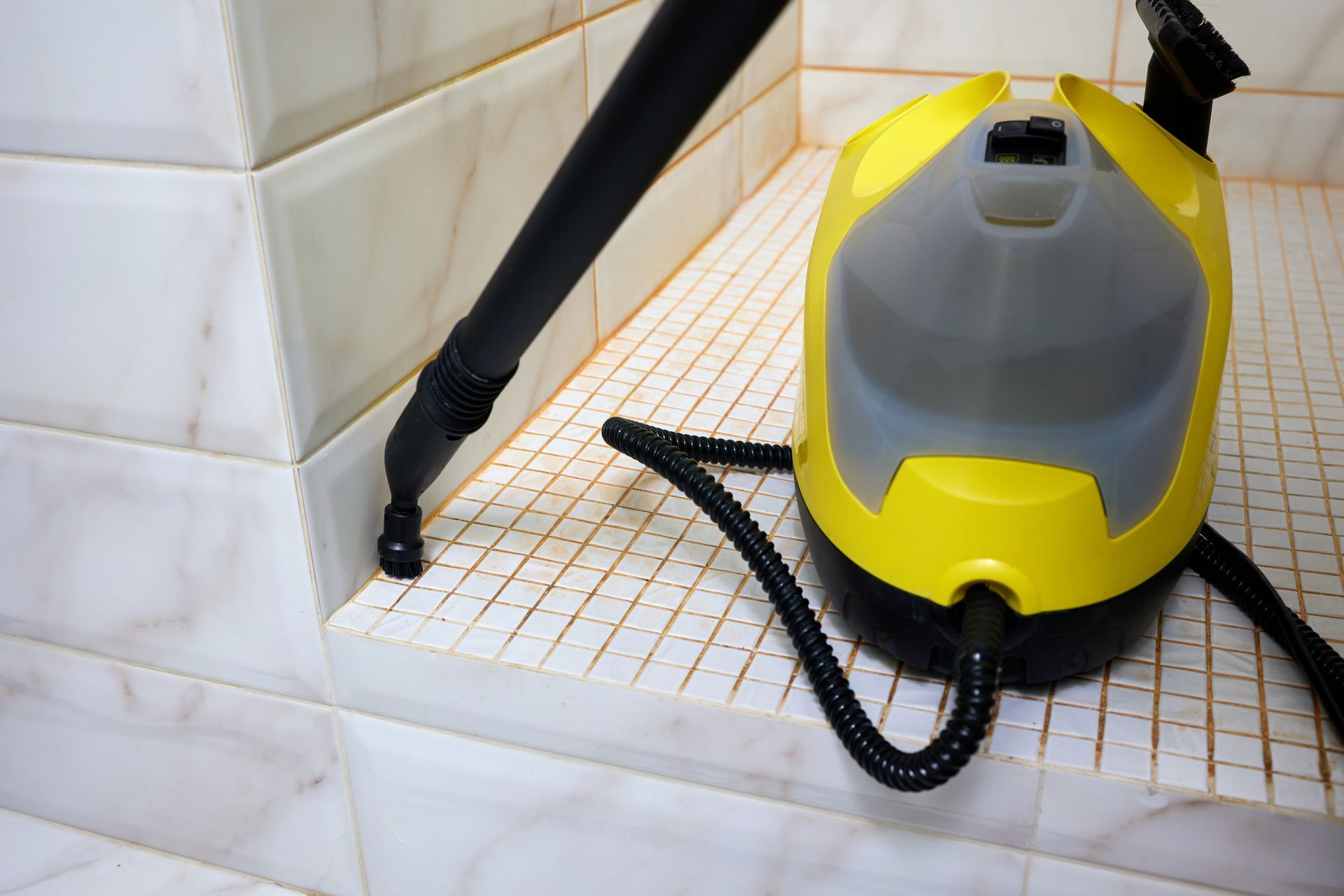 Yellow and gray steam cleaner on tiled bathroom step with black hose