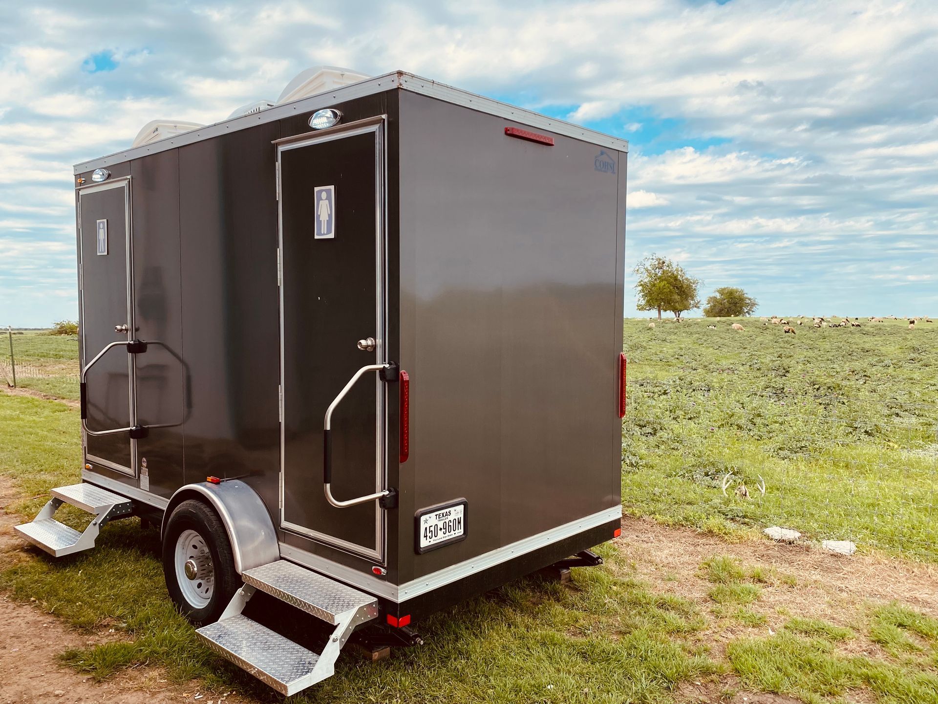 A trailer with a toilet on it is parked in a grassy field.