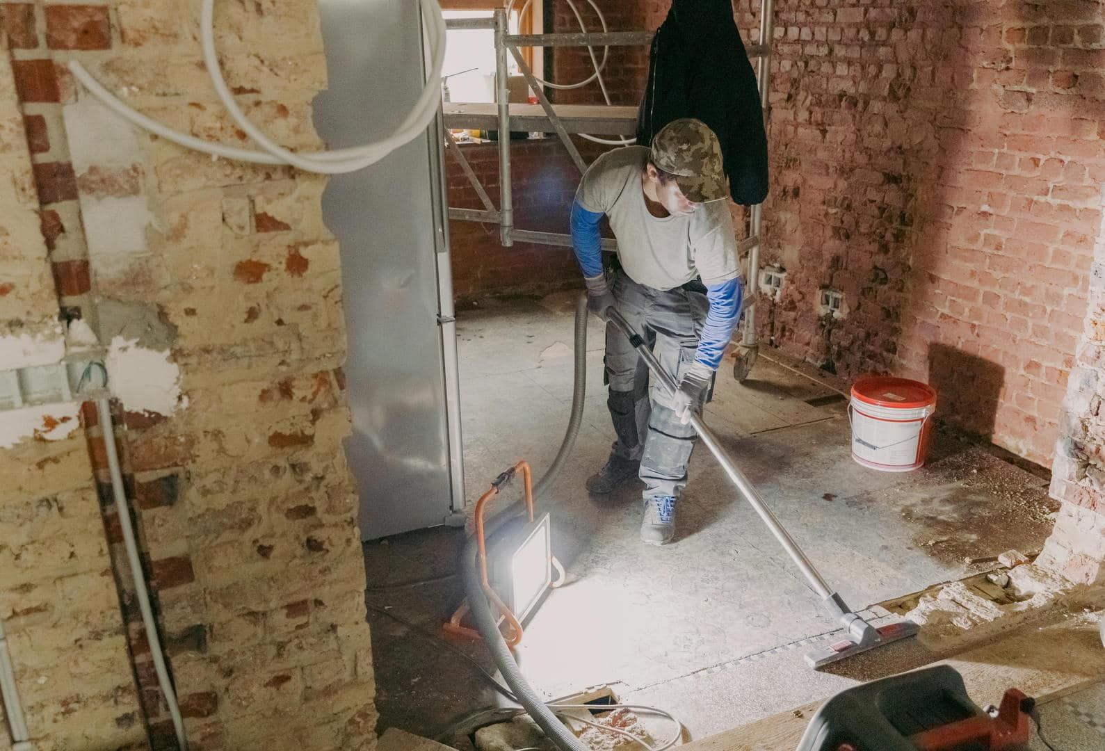 Person sweeping debris on a construction site, with brick walls, and work lights.