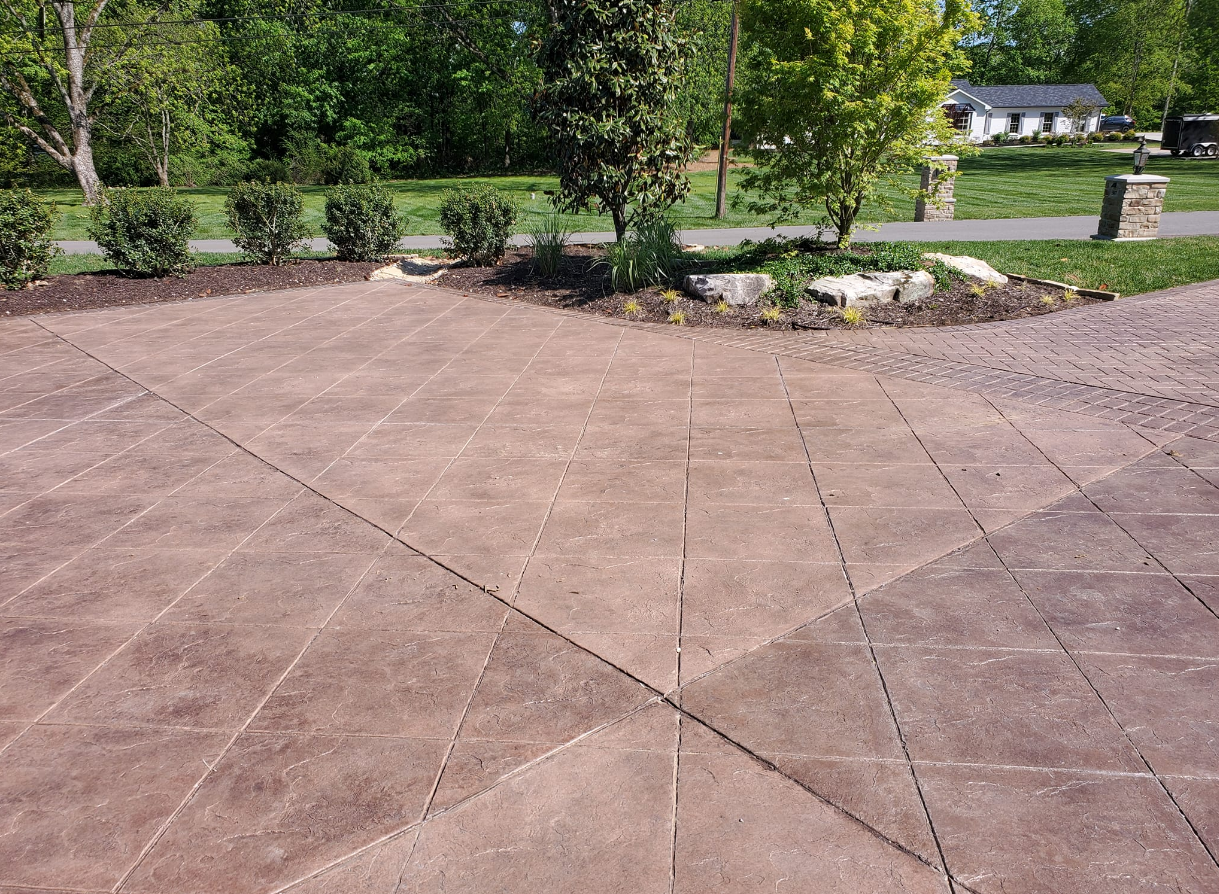 Brown patterned concrete patio with planted trees and bushes in a residential setting.