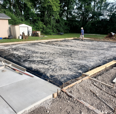 Construction site with a concrete slab, forms, and a worker.