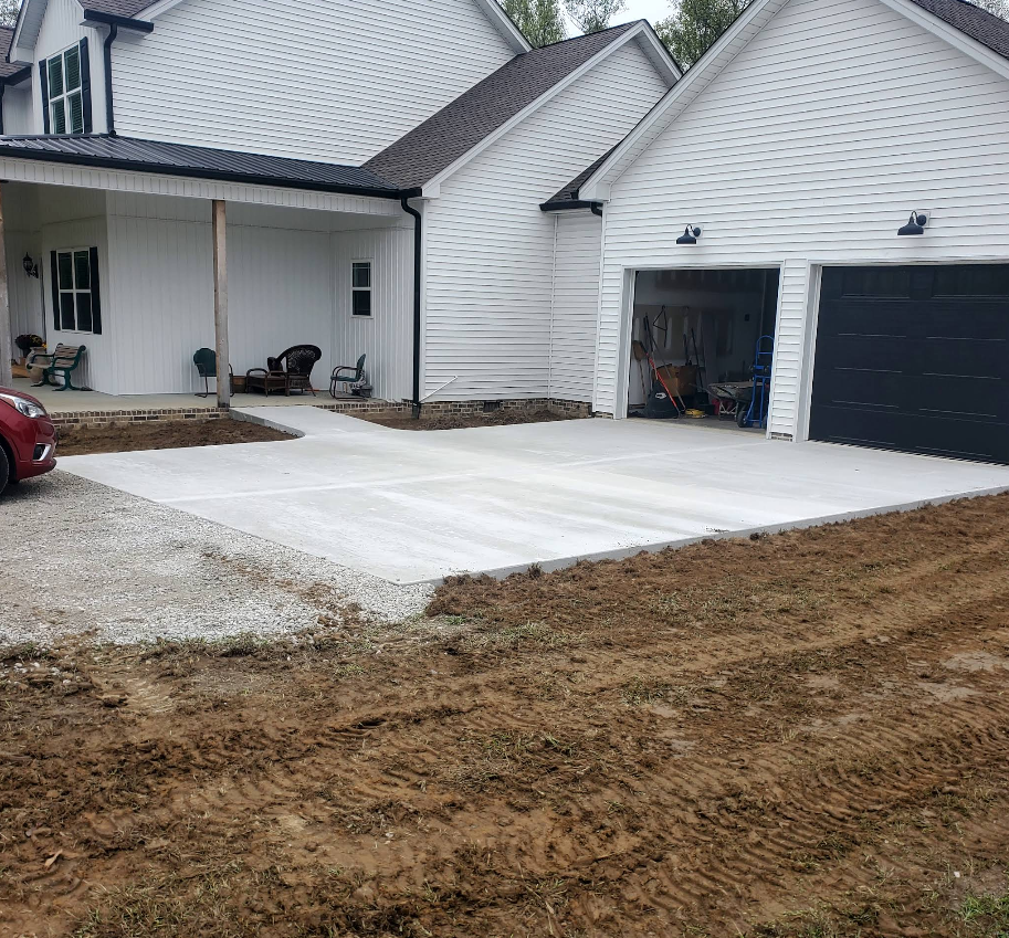 Newly poured concrete driveway in front of a white house with a garage and porch.