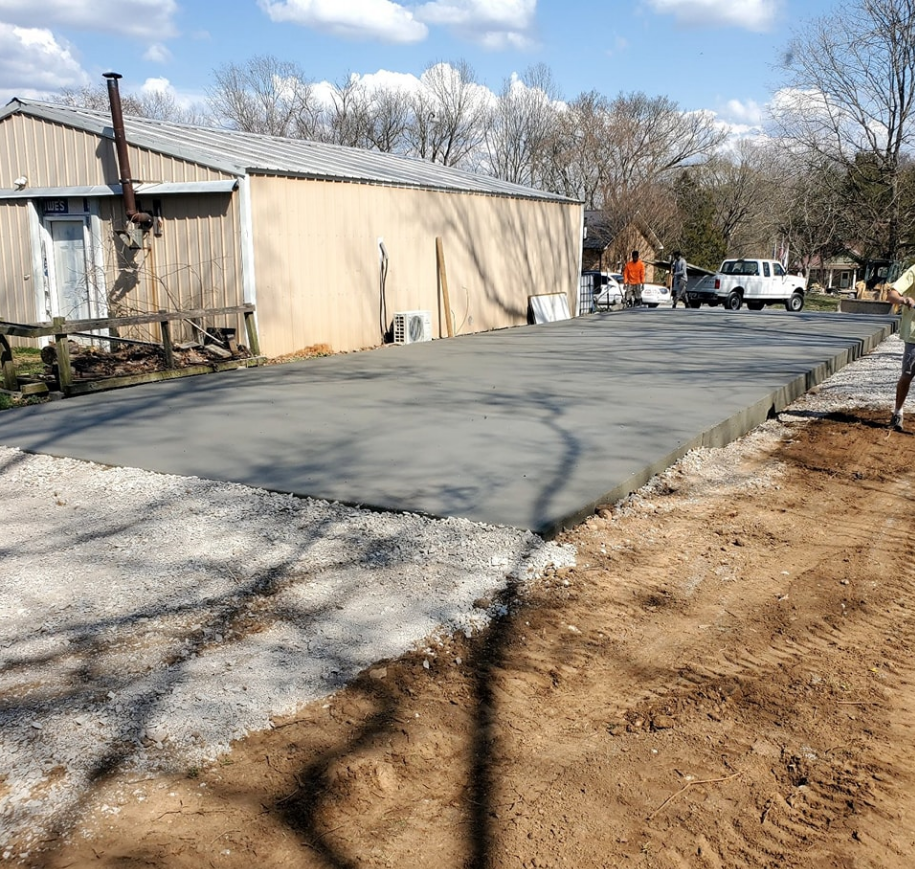 Newly poured concrete slab in front of a tan building. White gravel and dirt border the slab.