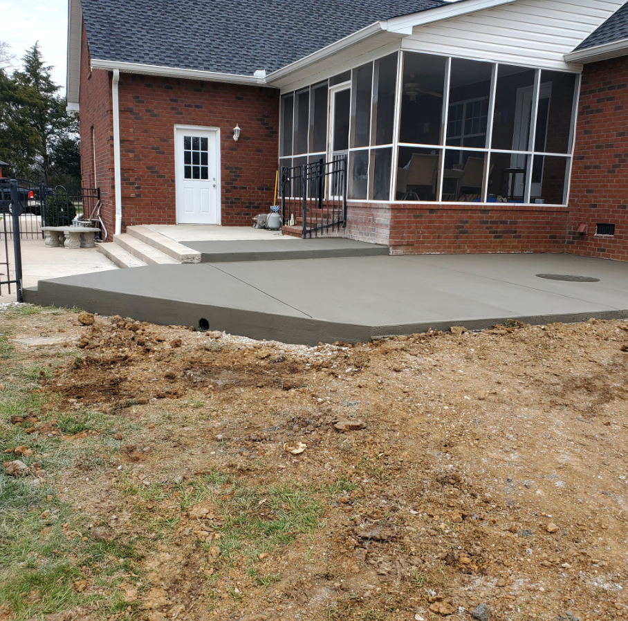 New concrete patio outside a brick house, near a screened porch and door.