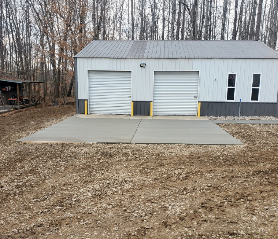 Garage with two doors, concrete pad, and gravel yard. Building has white walls, gray trim, and a metal roof.