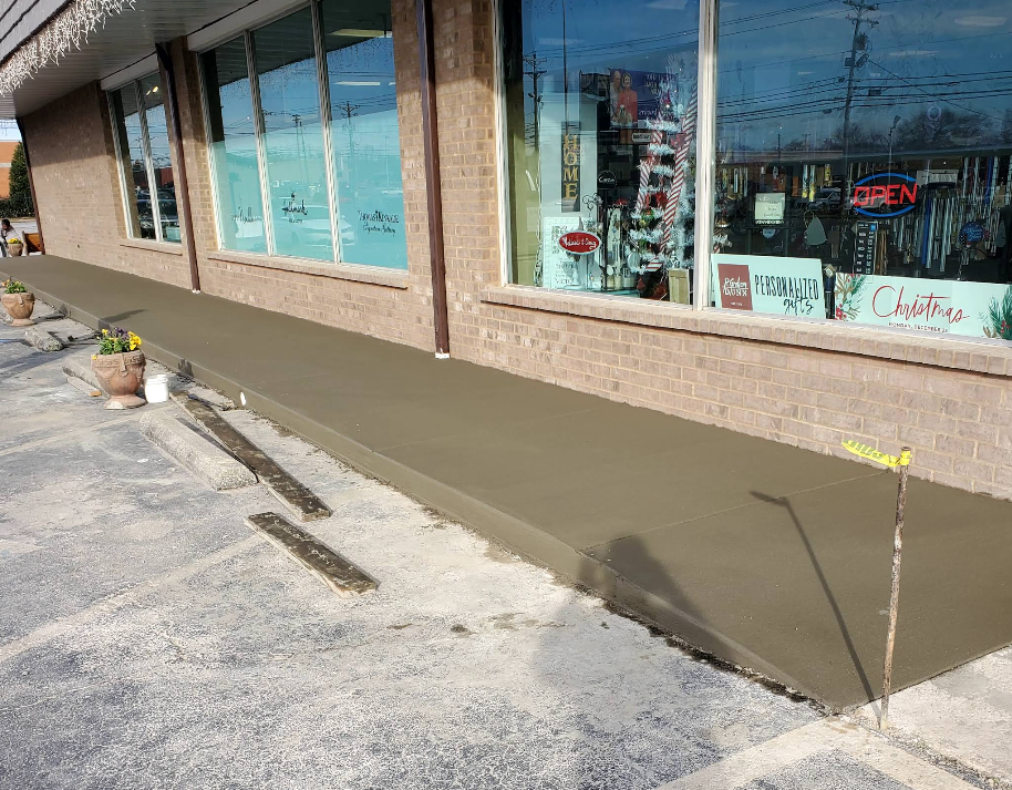 Newly poured concrete sidewalk outside a store with large windows.