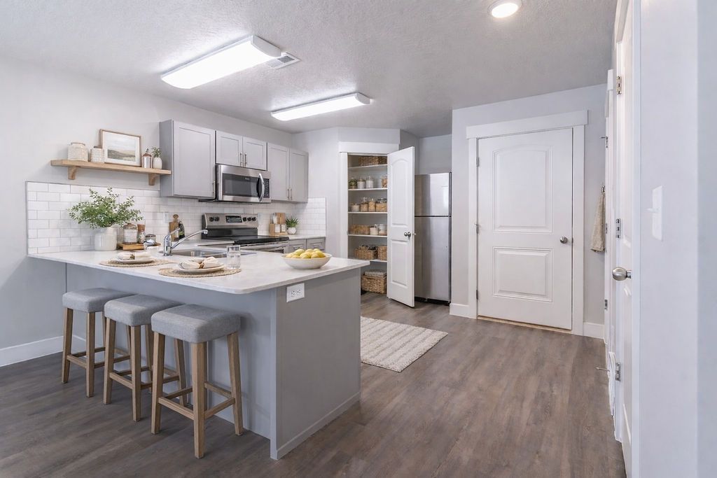 Bright modern kitchen with gray island, bar stools, white cabinets, and wood flooring